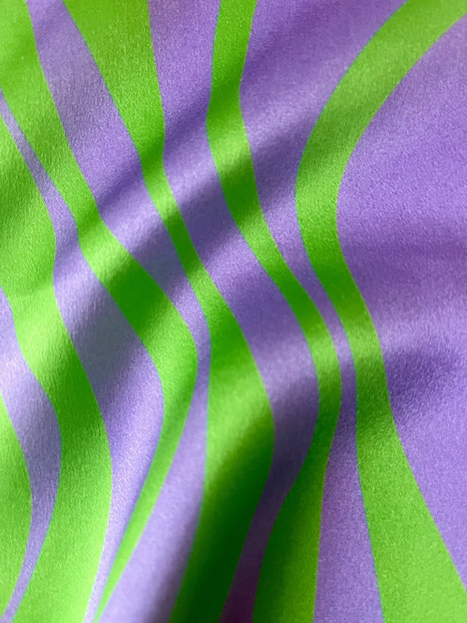 Close-up of a silk satin textile pattern with wavy stripes in green and purple