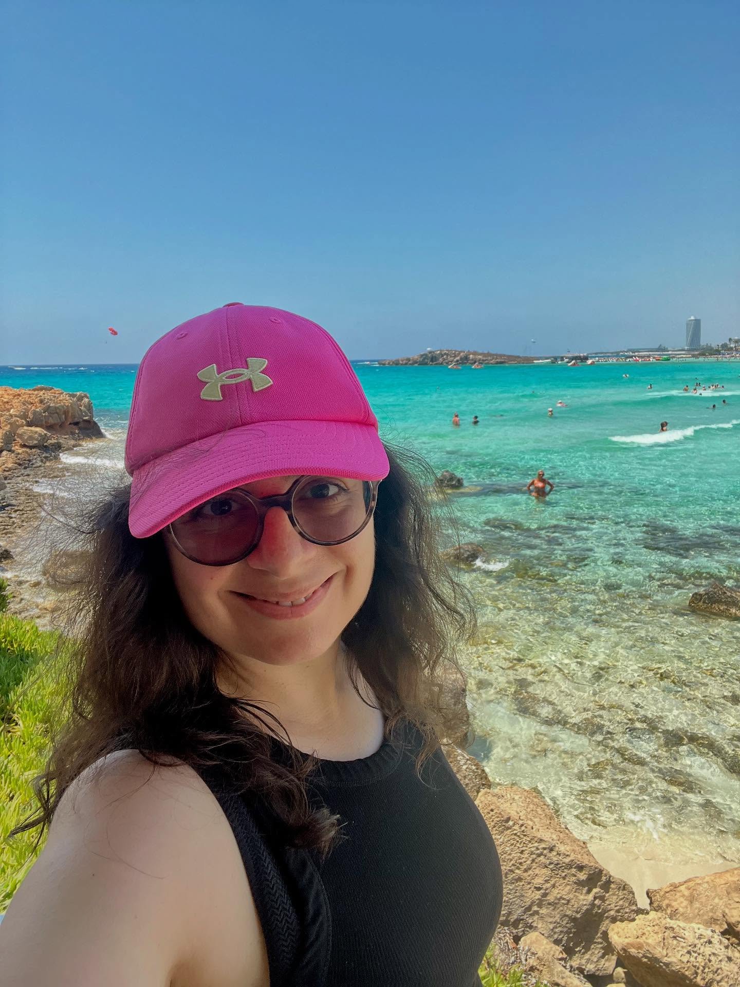 Woman pink cap beach selfie.