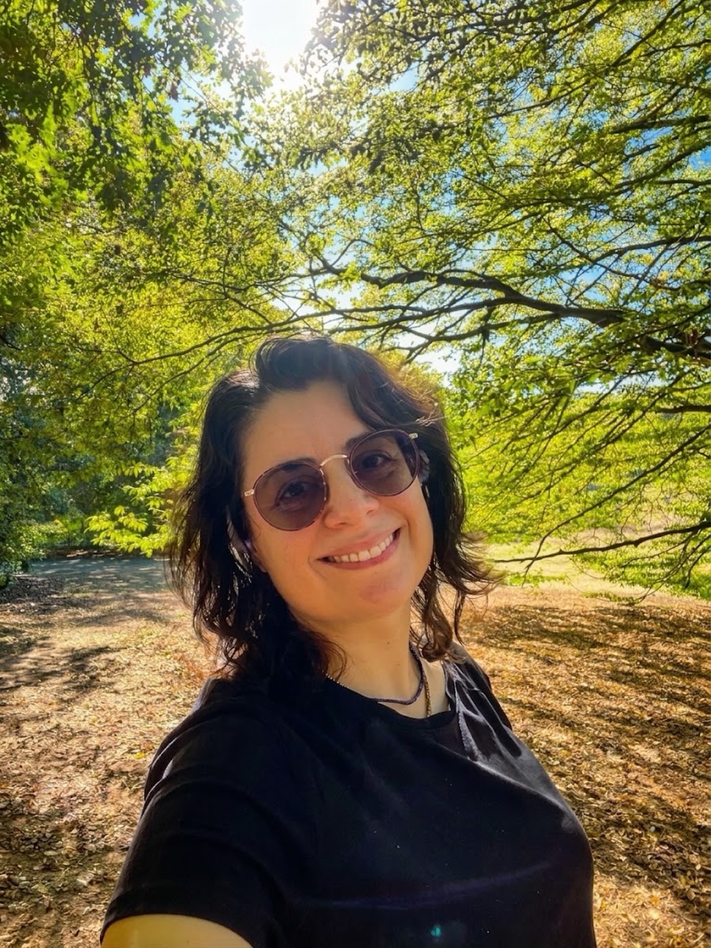 Kika Pierides smiling in a sunny London park during Thoughts On Walks: Returns to London — It’s a World.