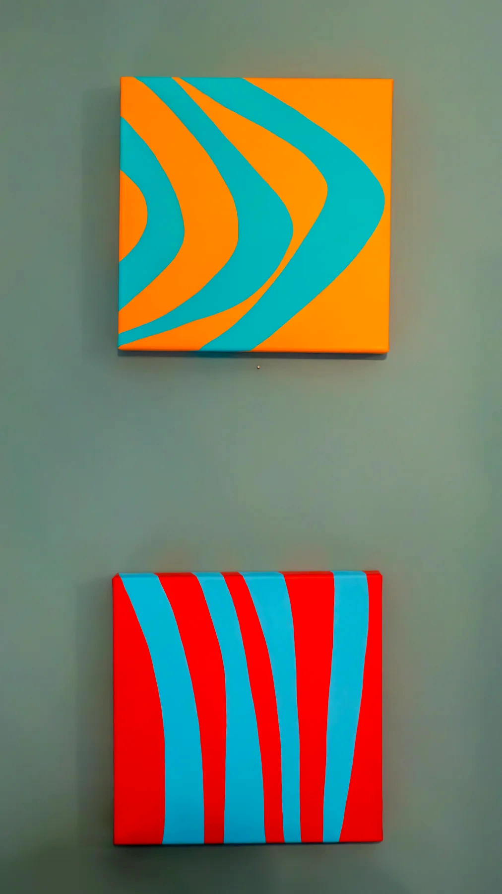 Two colourful paintings displayed one above the other on a formal wall