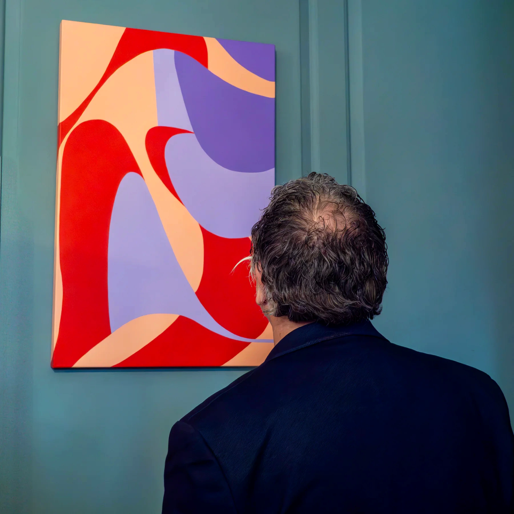 A visitor viewing a colourful red, lilac, and peach painting against blue-grey panelled walls