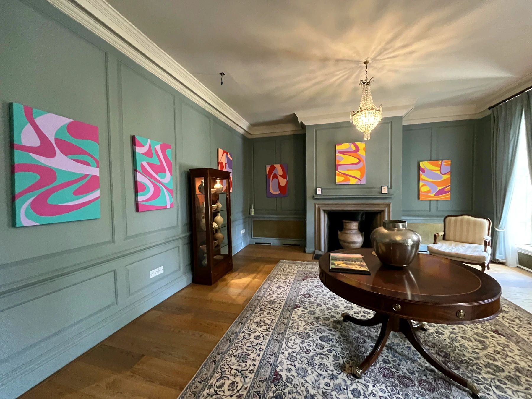 Colourful paintings installed throughout a formal room with blue-grey panelled walls